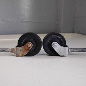 May include: Two black caster wheels with metal stems. One wheel has a rusty stem and the other has a silver stem.