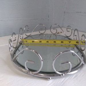 May include: A silver mirrored tray with a decorative scrolled rim. The tray measures 10 inches in diameter.