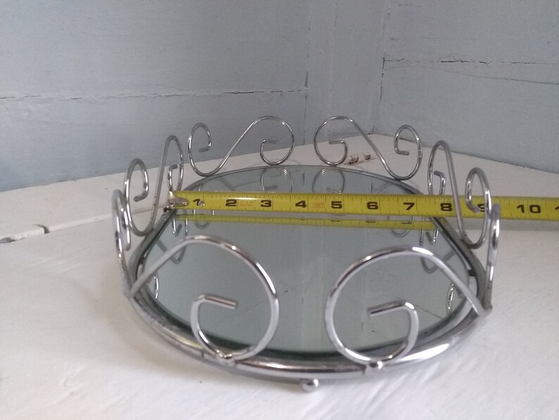 May include: A silver mirrored tray with a decorative scrolled rim. The tray measures 10 inches in diameter.