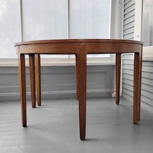 May include: A round wooden dining table with a smooth, polished finish in a medium brown tone. The table features four straight, tapered legs that extend from the circular tabletop, providing a stable base for the elevated, flat surface area.