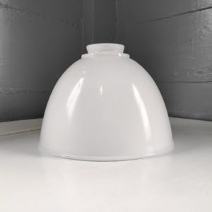 May include: A white, dome-shaped lampshade with a rounded top. The lampshade is made of a glossy material and sits on a white surface. The background is a gray corner.