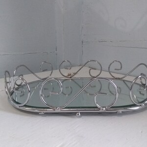May include: A silver oval tray with a mirrored surface and decorative scrollwork around the edge.