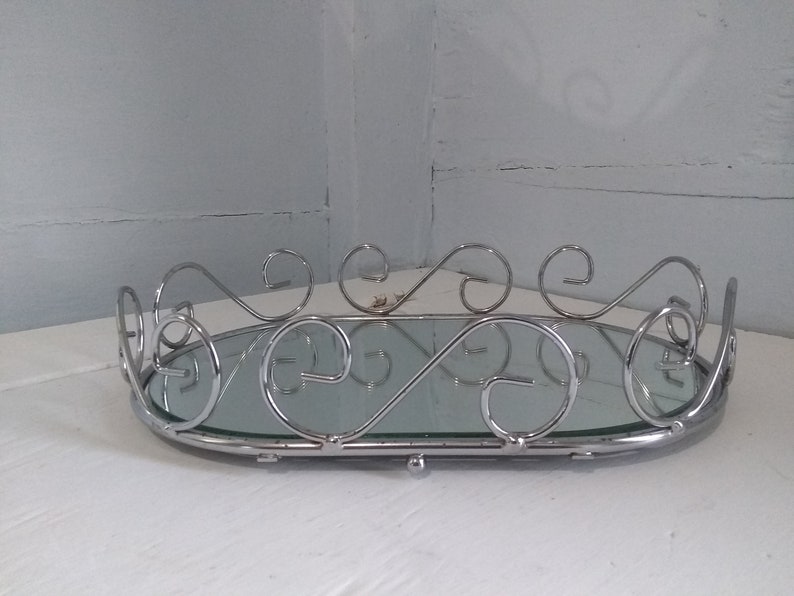 May include: A silver oval tray with a mirrored surface and decorative scrollwork around the edge.