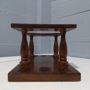 May include: A wooden wine bottle stand with four turned legs and a rectangular base. The stand has three circular cutouts for holding wine bottles.
