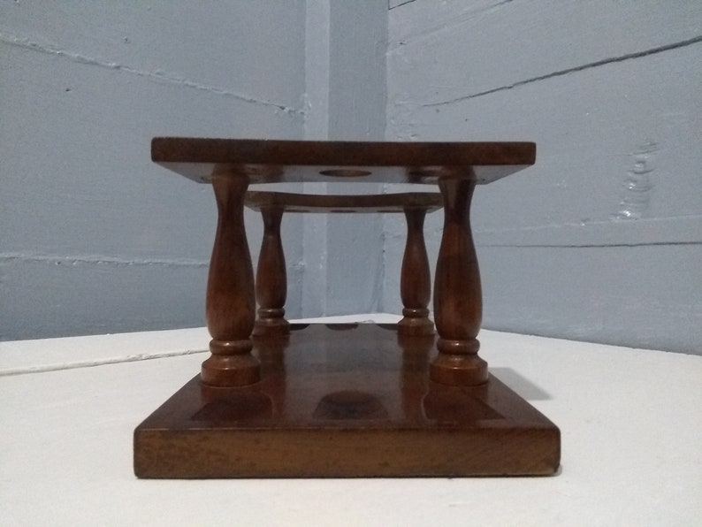 May include: A wooden wine bottle stand with four turned legs and a rectangular base. The stand has three circular cutouts for holding wine bottles.