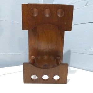 May include: A wooden wall-mounted rack with three round holes and a curved bottom shelf. The rack is made of dark brown wood and has a rustic look.