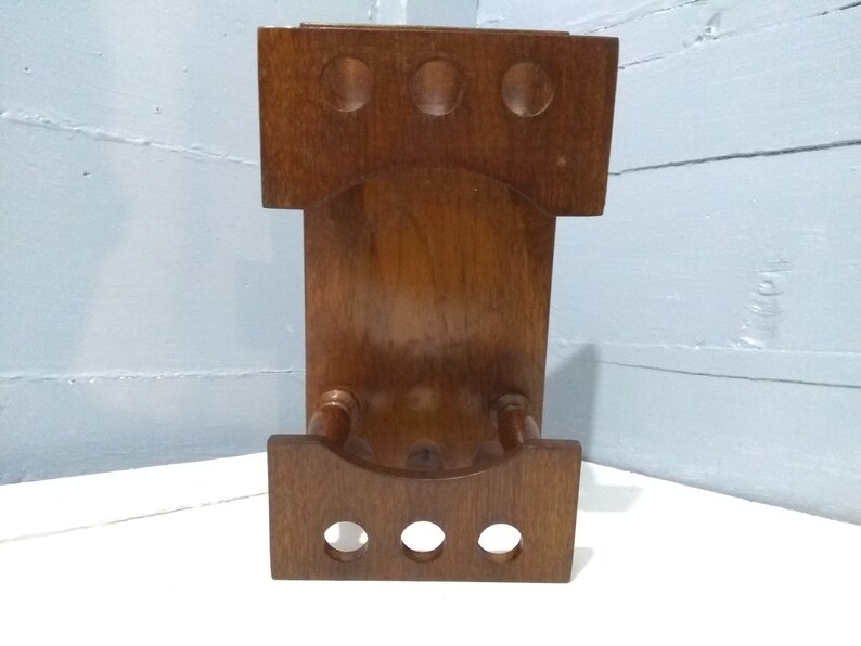 May include: A wooden wall-mounted rack with three round holes and a curved bottom shelf. The rack is made of dark brown wood and has a rustic look.