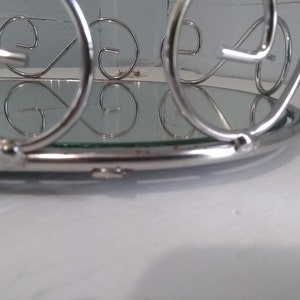 May include: A silver metal tray with a mirrored surface and decorative scrollwork around the edge.