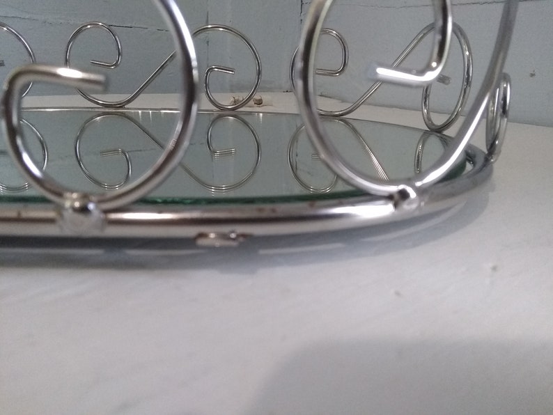 May include: A silver metal tray with a mirrored surface and decorative scrollwork around the edge.