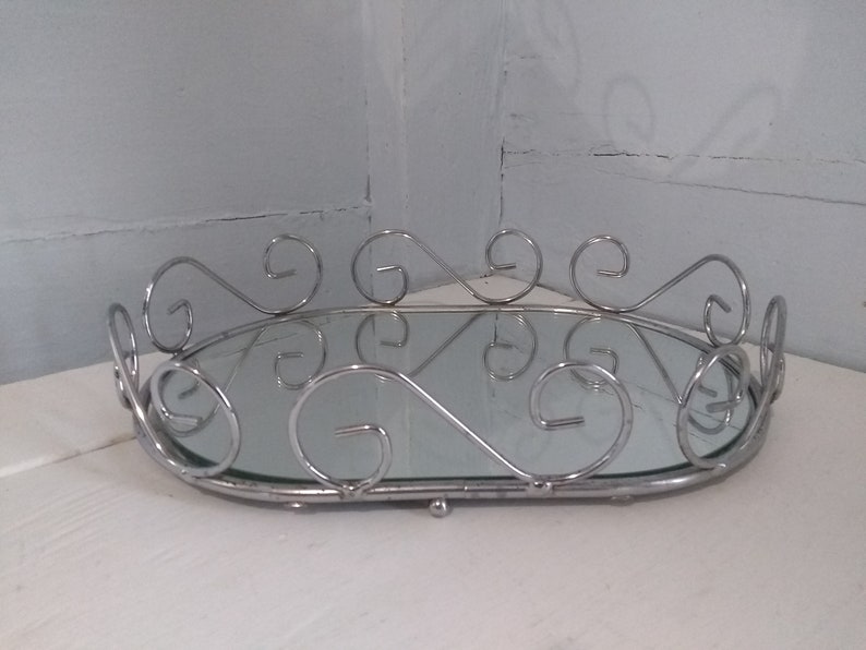 May include: A silver oval tray with a mirrored surface and a decorative scrolled rim.