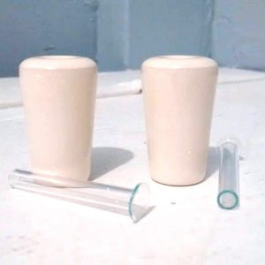 May include: Two white ceramic bottle stoppers with a clear glass tube.