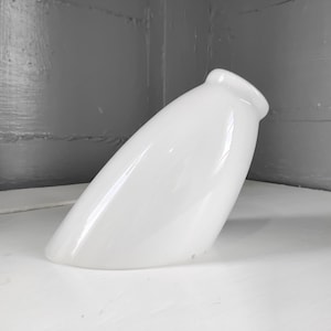 May include: A white, elongated vase with a rounded top and a smooth, glossy finish. The vase is angled, showcasing its sleek, modern design. The object is set against a neutral background, highlighting its form.