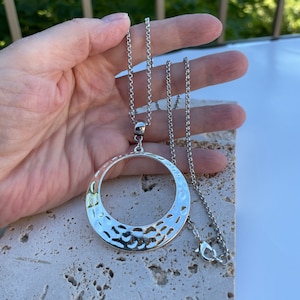 May include: A silver chain necklace with a large, hammered, circular pendant.