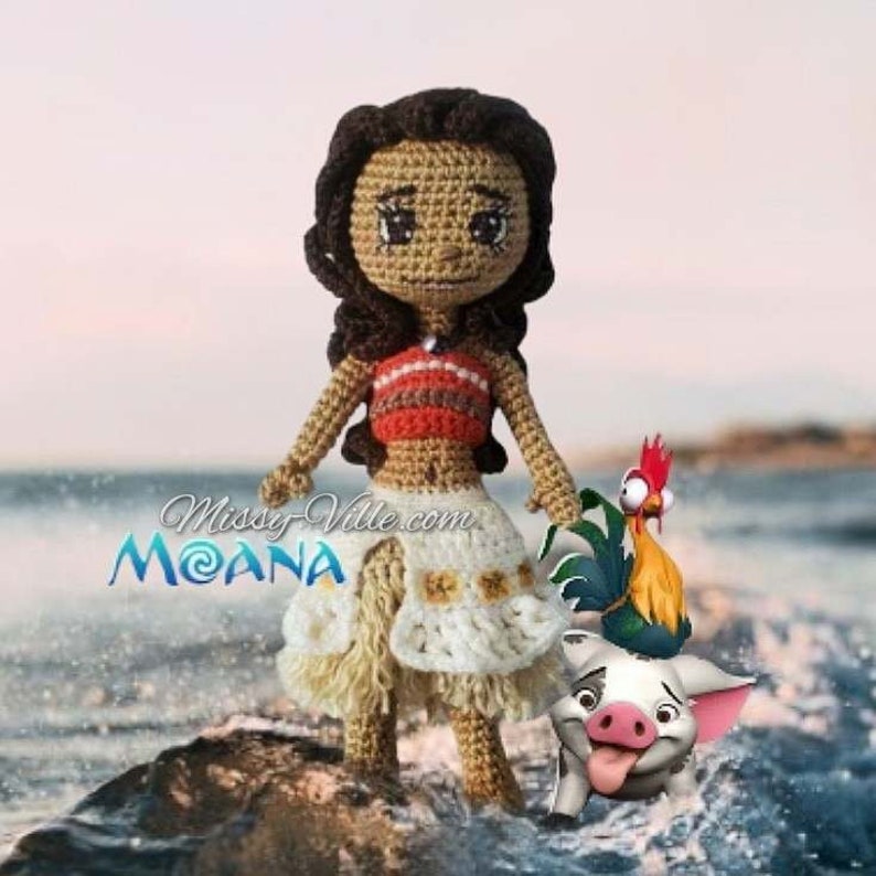 May include: Crocheted Moana doll with a brown and white skirt, a red and orange top, and brown hair. She is standing on a rock with a rooster and a pig beside her. The text "Missy-Ville.com MOANA" is visible in the background.