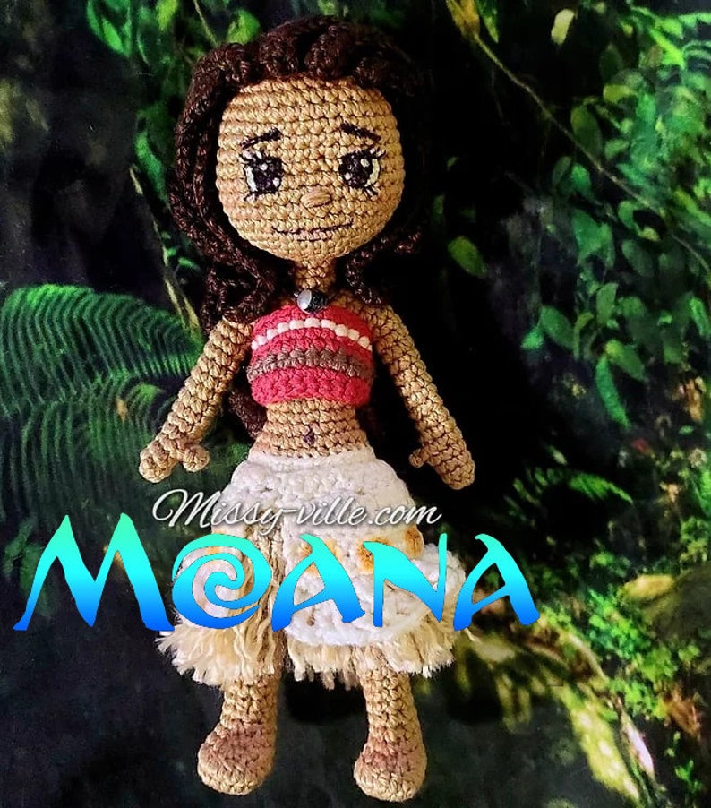 May include: Crocheted Moana doll with brown hair, a red and white top, and a white and brown skirt. The doll is standing on a green background with the text "Missy-ville.com MOANA" below it.
