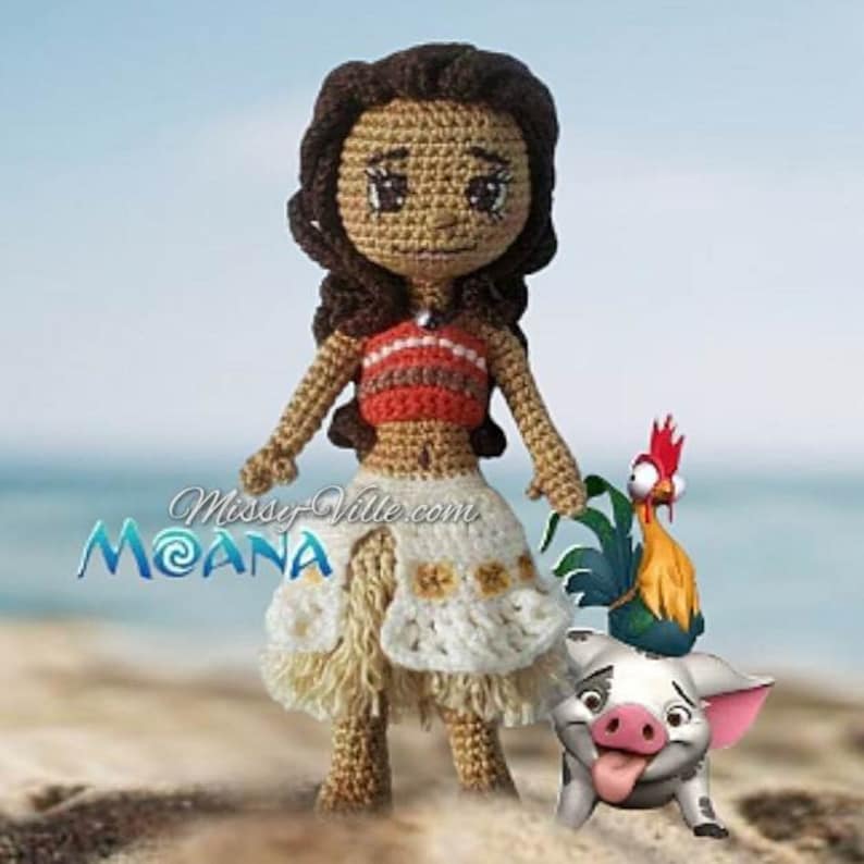 May include: Crocheted Moana doll with brown hair, a red and orange top, and a white skirt. She is standing next to a crocheted pig and a rooster.
