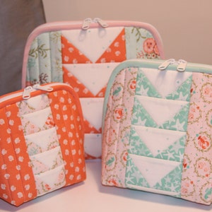 May include: Three quilted zippered pouches in different sizes. The largest pouch is teal and pink with a white background and a pattern of seashells and starfish. The medium pouch is orange and white with a pattern of white polka dots. The smallest pouch is orange and white with a pattern of white flowers.