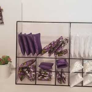 May include: A clear acrylic shelf unit with 12 compartments, filled with purple and white fabric squares. The squares are arranged in a grid pattern. The shelf unit is on a white surface.