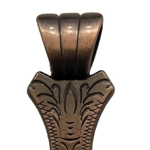 May include: Bronze-colored pendant with an ornate design. The pendant features a decorative top, a central section with etched patterns, and a bottom with a circular opening. The overall design is symmetrical and detailed, with a vintage aesthetic.