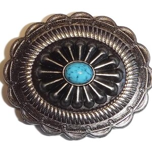 May include: A silver-toned metal belt buckle with a turquoise stone in the center. The buckle is decorated with a floral design and a scalloped edge.