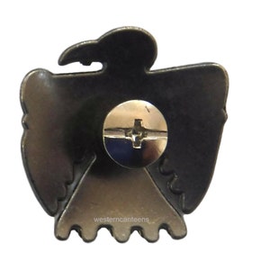 May include: The back of a metal eagle emblem with a screw for attaching it to a surface. The eagle is in a dark silver color and has a detailed design. The text "westerncanteens" is visible at the bottom.