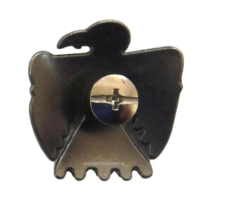 May include: The back of a metal eagle emblem with a screw for attaching it to a surface. The eagle is in a dark silver color and has a detailed design. The text "westerncanteens" is visible at the bottom.