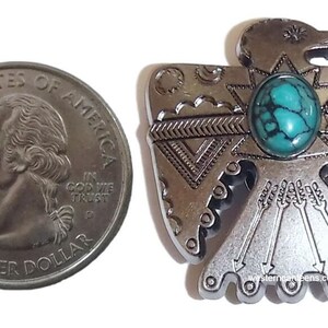 May include: Silver-toned metal Native American eagle pendant with a turquoise stone inlay. The eagle is depicted with outstretched wings and a detailed design.