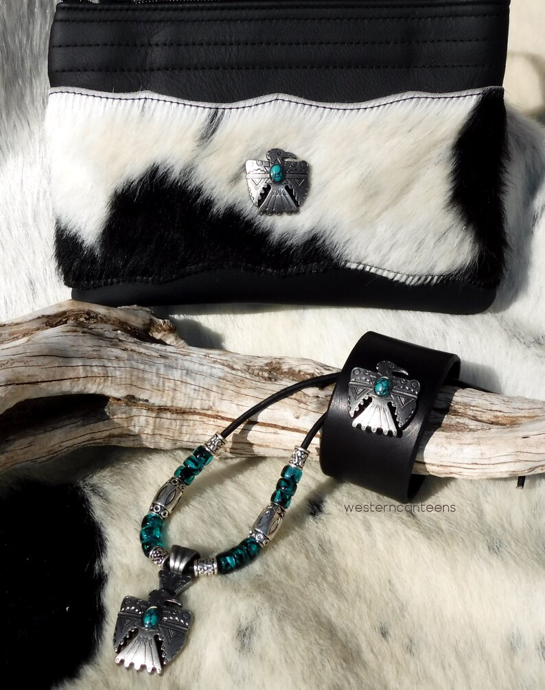 May include: A black leather wrist cuff with a turquoise and silver eagle design. A matching necklace with turquoise and silver beads and a pendant with a turquoise and silver eagle design. The jewelry is on a white and black cowhide background.