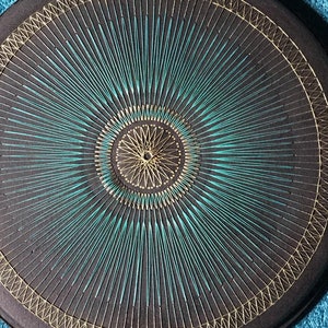 May include: A round black and gold decorative wall hanging with a turquoise starburst design.