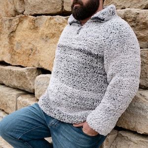 May include: A gray and white fuzzy pullover sweater with a zippered neck. The sweater is worn over a pair of blue jeans.