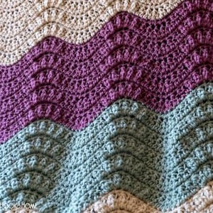 May include: A crocheted blanket with a wavy pattern in shades of cream, purple, and teal.