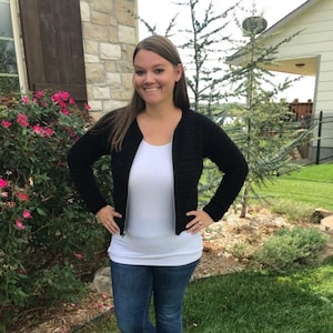 May include: A black crocheted zip-up jacket with long sleeves. The jacket is worn over a white tank top and blue jeans.