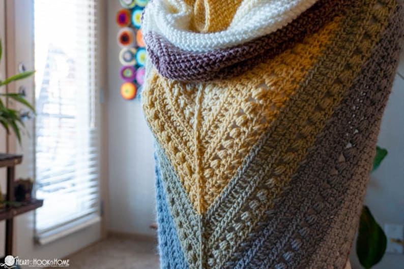 May include: A crocheted shawl with a gradient of blue, green, yellow, and white. The shawl is draped over a form and has a textured stitch pattern.