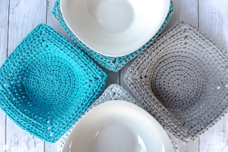 May include: Four crocheted pot holders in teal and gray, with white bowls on top. The pot holders are square and have a circular design in the center.