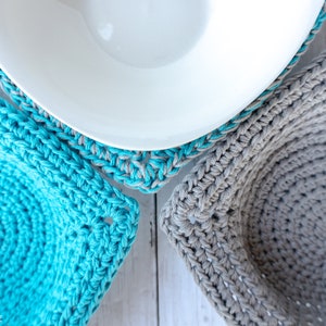 May include: Three crocheted bowl cozies in different colors and patterns. One is gray, one is turquoise, and one is a turquoise and gray combination.