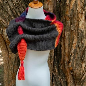 May include: A dark gray knitted cowl scarf featuring a vibrant gradient of red, orange, and purple along the edges. The scarf has a textured stitch pattern and includes a long, tapered tail that ends in a matching red yarn tassel.