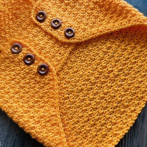 May include: A yellow crocheted blanket with a textured stitch pattern and brown buttons.