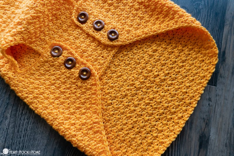 May include: A yellow crocheted blanket with a textured stitch pattern and brown buttons.