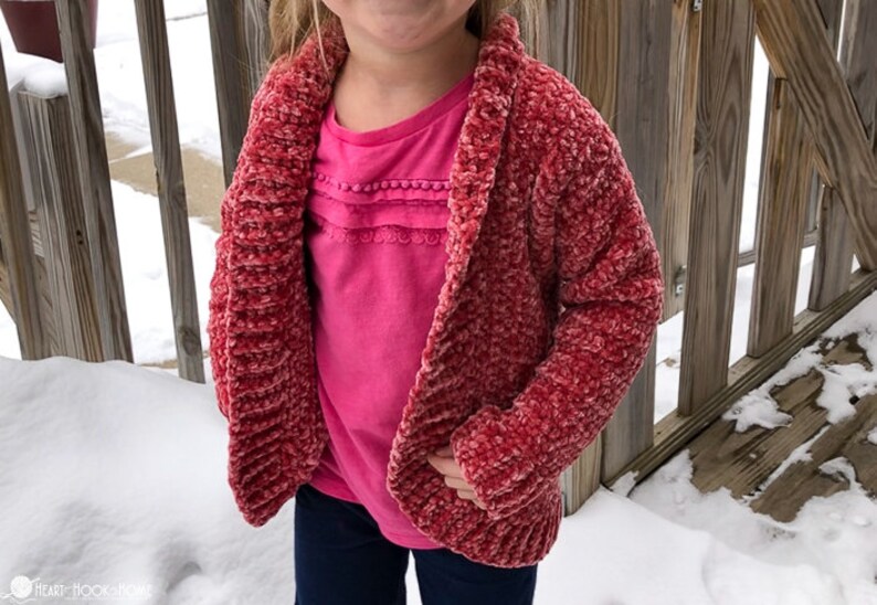 May include: A red crocheted cardigan with a shawl collar. The cardigan is made with a fuzzy yarn and has a slightly textured look.