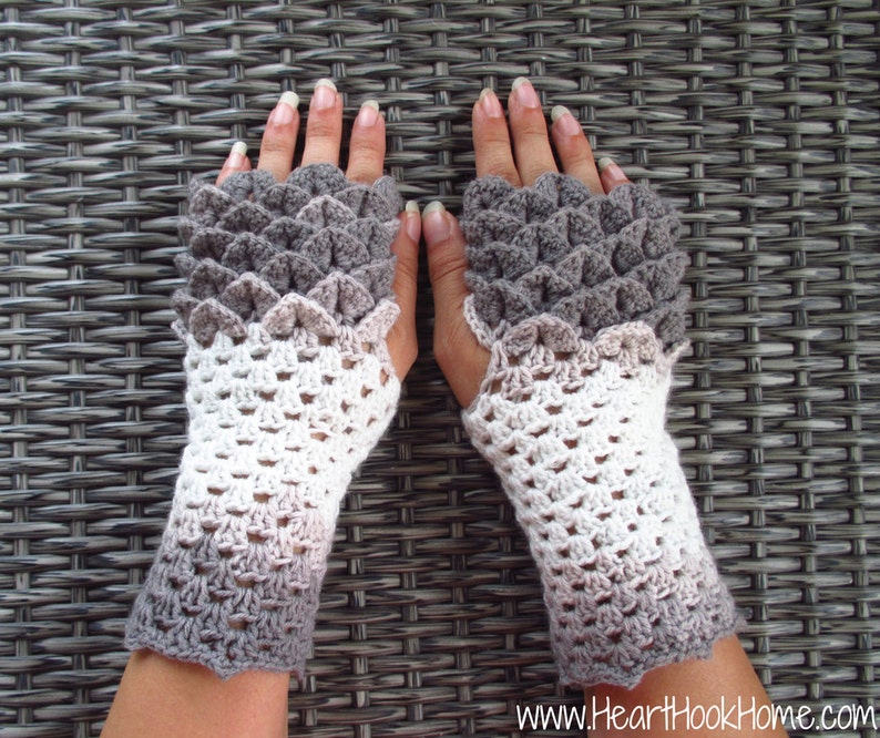 May include: A pair of grey and white crocheted fingerless gloves with a scale pattern on the top of the hand.