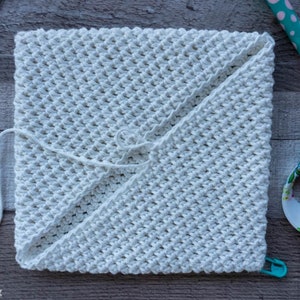 May include: A white crocheted square with a textured pattern. The square is folded in half and secured with a white string.