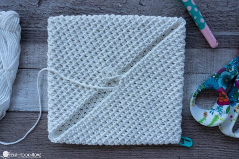 May include: A white crocheted square with a textured pattern. The square is folded in half and secured with a white string.