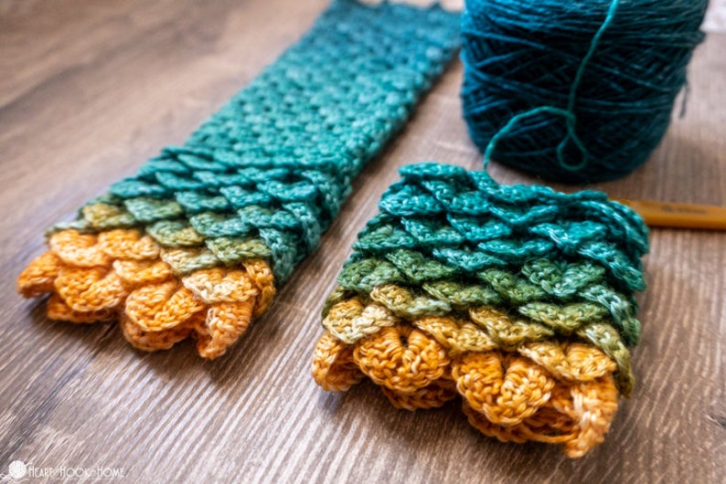 May include: A close-up of a crocheted scarf with a dragon scale pattern in shades of green, yellow, and orange. The scarf is made with a gradient yarn and is lying on a wooden surface.