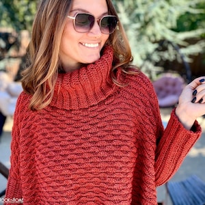 May include: A rust-colored, long-sleeved, crocheted sweater featuring a prominent ribbed turtleneck collar and a textured, repeating wave-like stitch pattern throughout the body. The garment has long sleeves with ribbed cuffs.