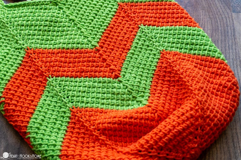 May include: A handmade crochet blanket in a vibrant color scheme of green and orange. The blanket features a geometric design with alternating bands of the two colors, creating a textured and visually appealing pattern. The stitches are tightly woven, suggesting a durable and cozy item.