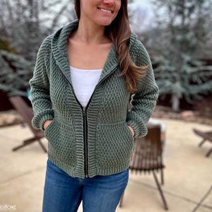 May include: A green hooded sweater with a zipper closure and pockets. The sweater is made of a textured knit fabric.