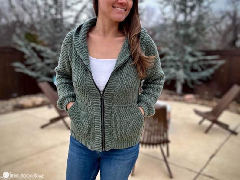 May include: A green hooded sweater with a zipper closure and pockets. The sweater is made of a textured knit fabric.