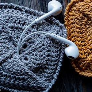 May include: Two crocheted coasters, one gray and one mustard yellow, with white earbuds resting on top.