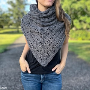 May include: A gray crocheted shawl with a lacy pattern and a textured design. The shawl is worn by a person with long brown hair and is draped around their neck.