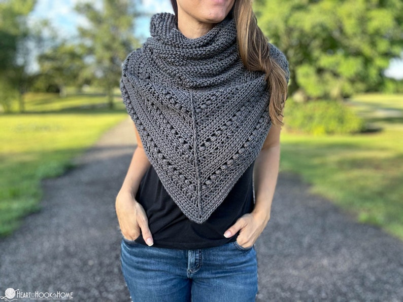May include: A gray crocheted shawl with a lacy pattern and a textured design. The shawl is worn by a person with long brown hair and is draped around their neck.